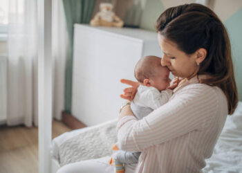 Mother holding her baby boy in arms at home by the window.